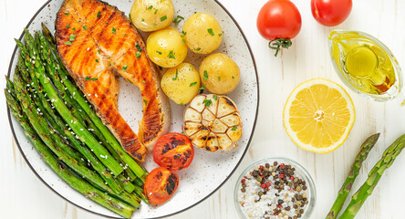 Plate of grilled trout steak, asparagus and potatoes on the white wooden table. Top view.