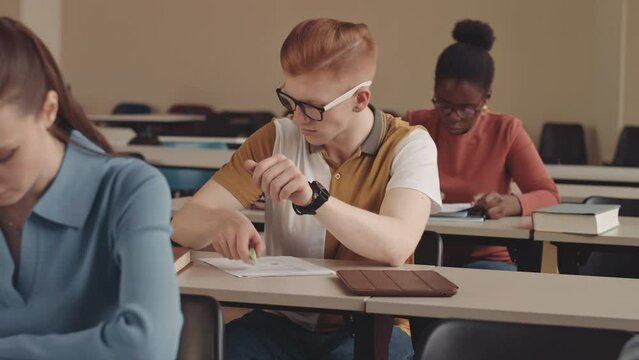 Waist up slowmo of Caucasian male college student using smartphone while doing test in class