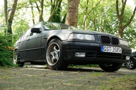 Low angle shot of tuned BMW E36 black matte sedan with Polish numberplate in a forest
