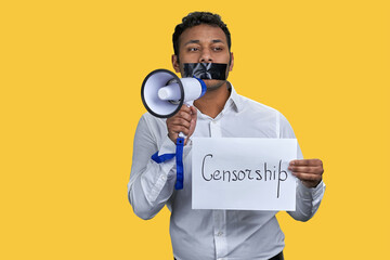 Young indian male with megaphone and word censorship. Vivid yellow background.