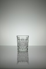 Crystal water glass reflecting on a gray surface with white background