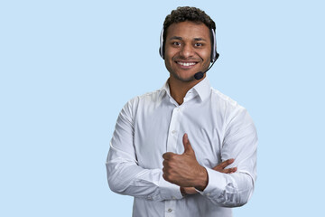 Portrait of a young smiling customer support worker. Indian man with headset. Pale blue background.