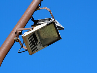 Old broken spotlight or lantern on a rusty pole against a blue sky