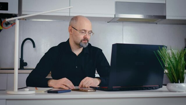 Handsome online baseman in glasses relaxing working at laptop explain on video meeting for creative team concept of project. Busy worker freelancer entrepreneur working home at kitchen in financial