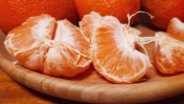 Segments of tangerine and whole fruits on wooden dish