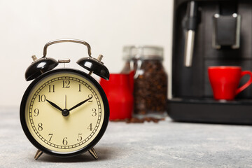 Alarm clock and a cup of morning coffee with a coffee machine on the background of the kitchen interior.A glass of coffee on the table with a clock in the morning. Good morning concept. WAKE UP! 
