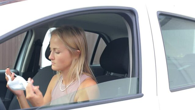 A young girl with allergies puts on a mask and closes the car window. Caucasian sleepy attractive young woman in car.
