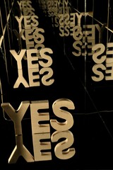 Vertical view of a wooden block spelling out YES reflecting in glass mirrors