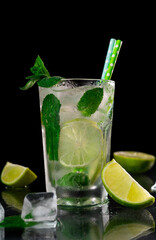 Refreshing Mojito Cocktail with lime, ice cubes and green mint leaves on a black background