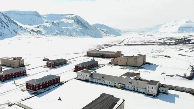 Drone shot of the snow covering the houses, road and mountains of Pyramiden town in Spitsbergen