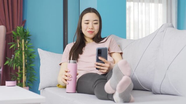 Happy asian young woman stretching on the sofa.
Young asian woman stretching on sofa at home.
