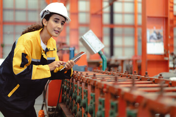 Latin woman engineer inspecting heavy machinery system in production line for manufacturing safety....