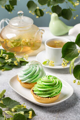 Tartlets with meringue and linden tea in a glass teapot, blossoming linden branches around. Herbal tea.