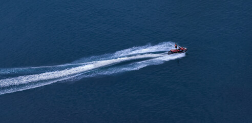 Naklejka premium The jet ski travels at great speed through blue water, leaving a foamy trail. View from above