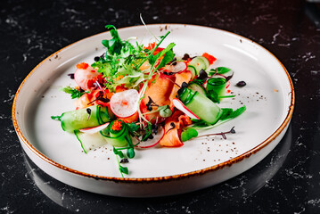 Green salad with salmon, cucumbers, lettuce, spices, caviar in plate