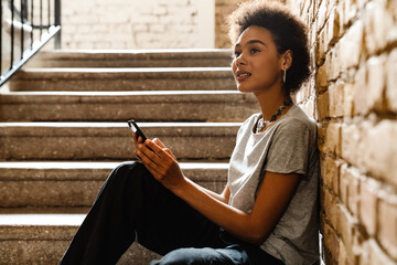 Young african woman using mobile phone while sitting on stairs