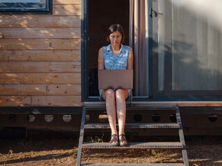 Happy young asian woman with laptop resting outdoors near tiny house, weekend away and remote...