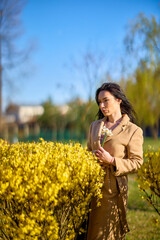 beautiful woman posing by a blooming yellow tree on a sunny spring day.