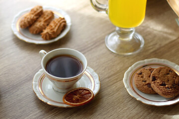 Cup of tea, plates with cookies, glass of orange juice, books, reading glasses, bowl of fruit and candles on the table. Selective focus.