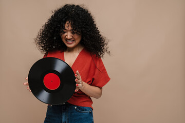Smiling asian woman posing with vinyl record isolated over beige background