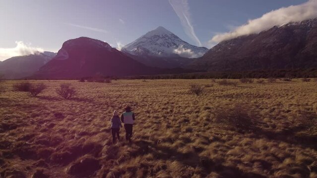 Aerial of a couple running in a field with the Lanin volcano against a blue sky in the background