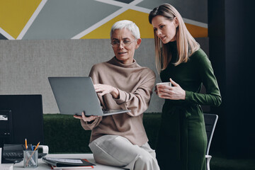 Two confident women using technologies and communicating while working in office together