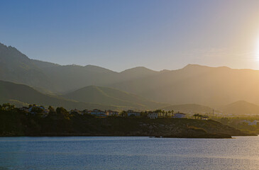 sunset on the sea bright sky with clouds on the left you can see the mountains no longer lit by the sun and the orientation is landscape there is a place for text