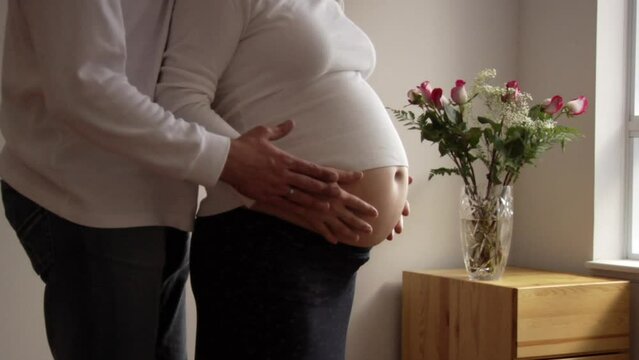 Pregnant woman rubbing her belly and her husband walking up to her