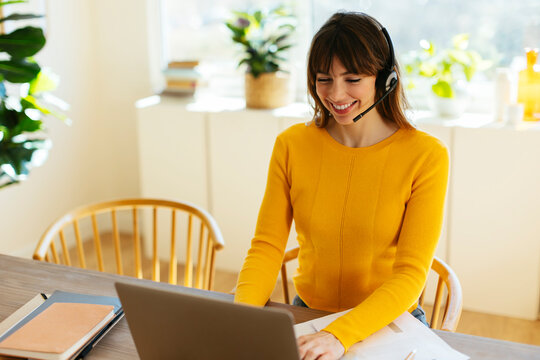 Happy freelancer wearing headset working on laptop at home office