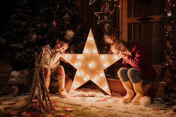 Girls leaning head on illuminated start shape light at Christmas