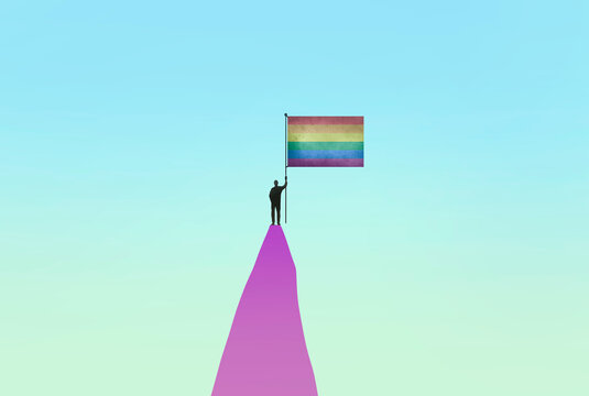 Person standing with rainbow flag on top of mountain peak