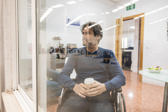 Thoughtful businessman with coffee cup sitting in wheelchair