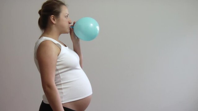 Pregnant woman blowing up a blue balloon