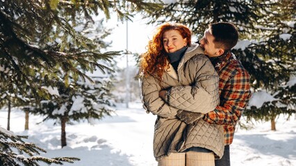 A smiling guy hugs his girlfriend who is cold after a long walk and wants to go home. A young red-haired girl is shivering in the cold while a guy hugs her to keep her warm.