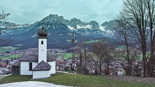 View over Ellmau from the hill with the little white chapel and the austrian alp mountains in the background.
