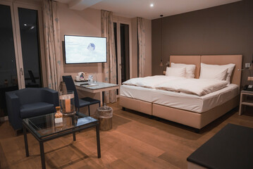 Duvet and pillows on bed in illuminated empty room of luxury hotel with television, luxury travel concept