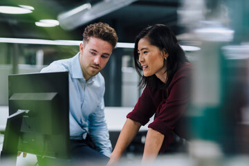 Young businessman discussing with colleague over desktop PC in office
