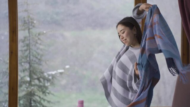Asian young woman watching snowfall through window.
A young Asian woman who is cold at home, puts on a shawl and watches the snow falling from outside.
