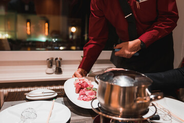 Midsection of waiter serving meat on a plate to customer sitting at the table in restaurant, luxury travel concept