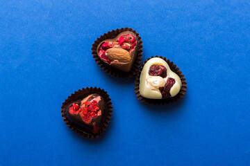 chocolate sweets in the form of a heart with fruits and nuts on a colored background. top view with space for text, holiday concept