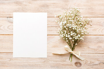Wedding mockup with white paper list and flowers gypsophila on colored table top view flat lay. Blank greeting cards and envelopes. Beautiful floral pattern. Flat lay style