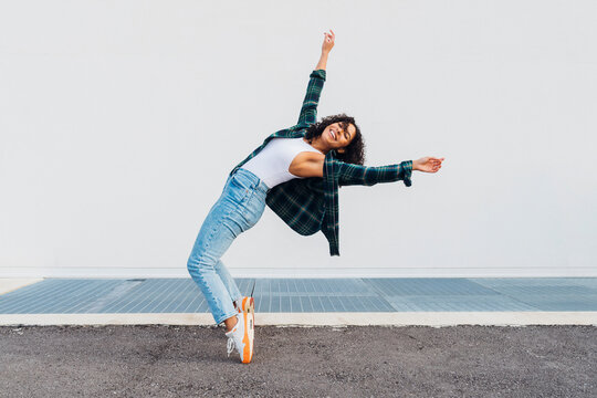 Happy woman dancing and bending over backwards in front of wall