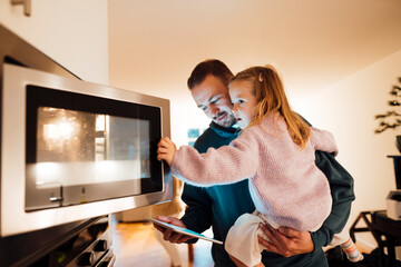 Father carrying daughter opening oven door in kitchen at home