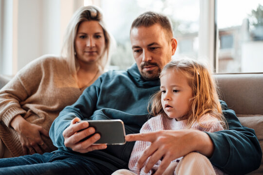 Father sharing mobile phone with daughter at home