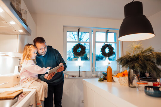 Father sharing tablet PC with daughter sitting on kitchen counter at home
