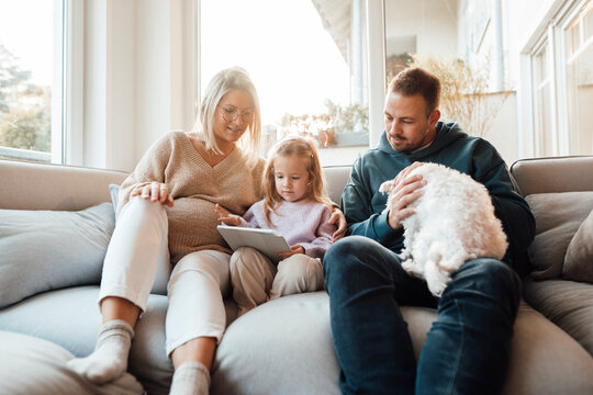 Girl using tablet PC sitting by parents and dog at home