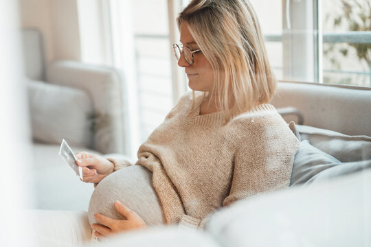 Woman with blond hair holding ultrasound photo at home