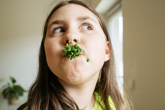 Girl eating microgreens in kitchen at home