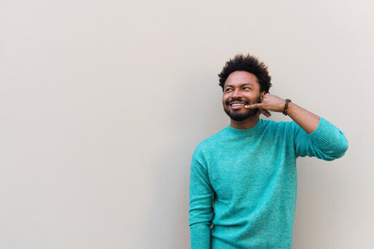 Smiling man making calling gesture in front of wall