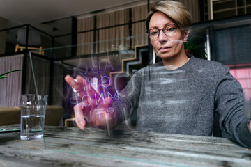 Woman wearing eyeglasses touching transparent glass screen at home